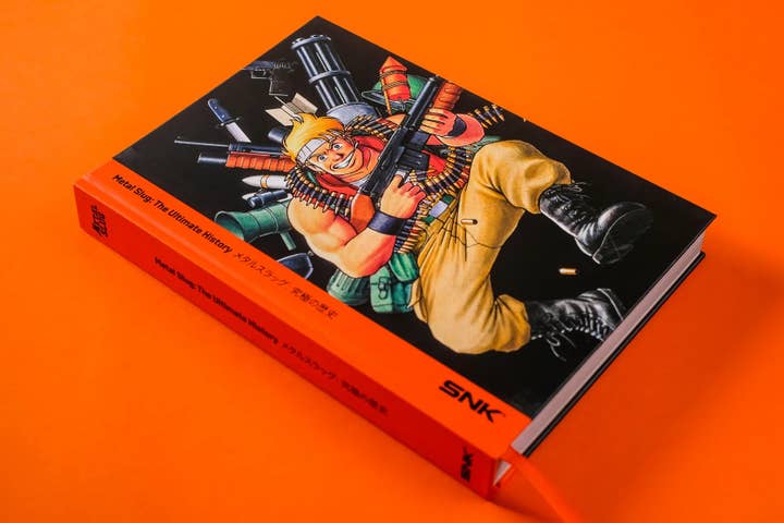 A photograph of a thick book on an orange background. The cartoon character on the front is holding a gun and is surrounded by stylized weapons.